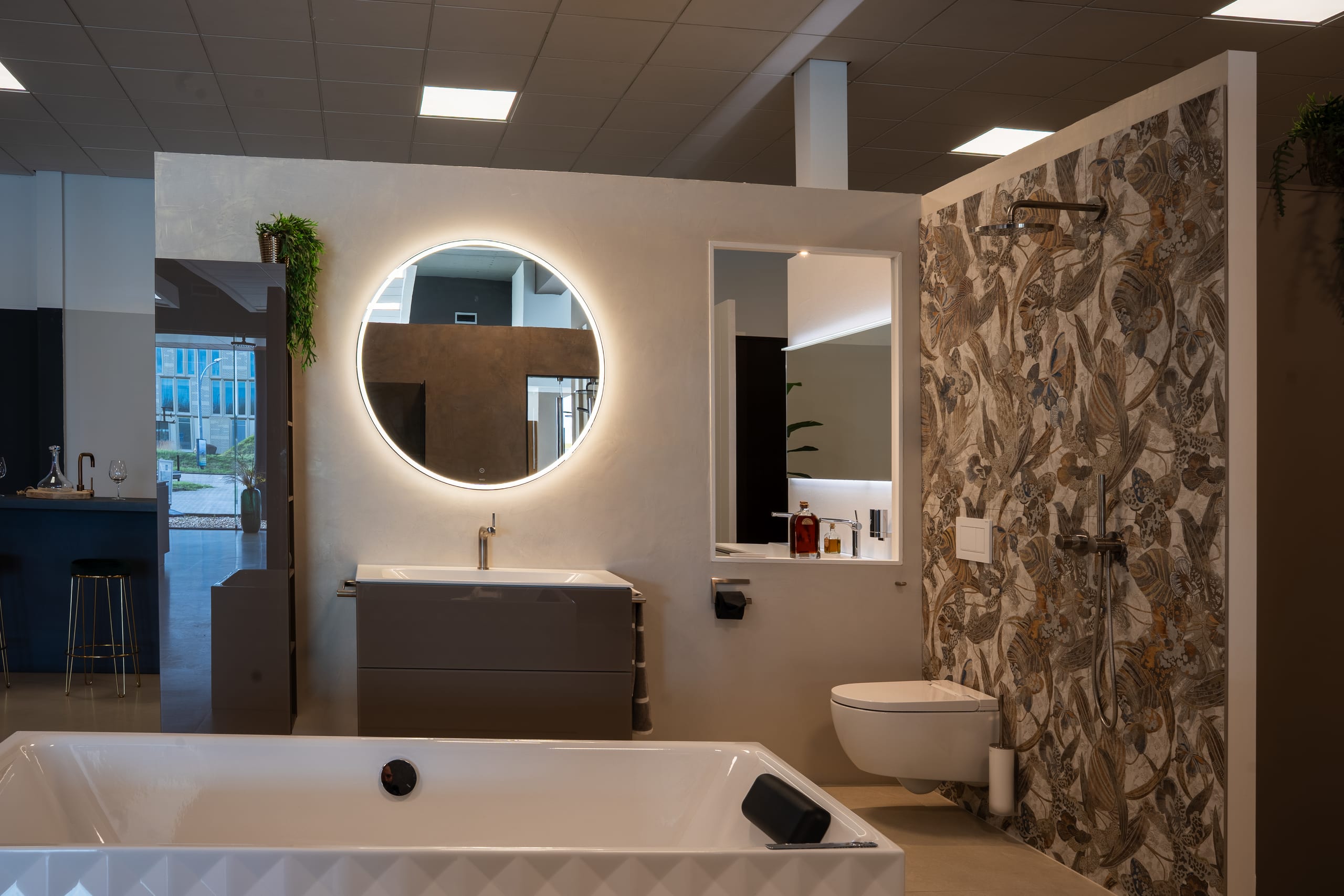 Showroomopstelling badkamer met botanisch behang, verlichte ronde spiegel en vrijstaand bad